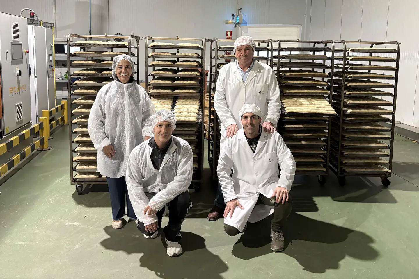 Imagen de la familia Barcos (mujer, marido y dos hijos) en la nave de la empresa familiar con bandejas de pan en carritos metálicos.