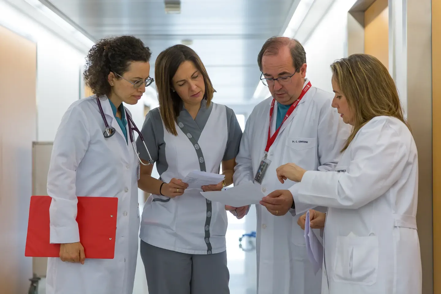 Imagen de una enfermera, un médico y dos doctoras consultando unos documentos de pie en un pasillo de hospitalización de la Clínica Universidad de Navarra.