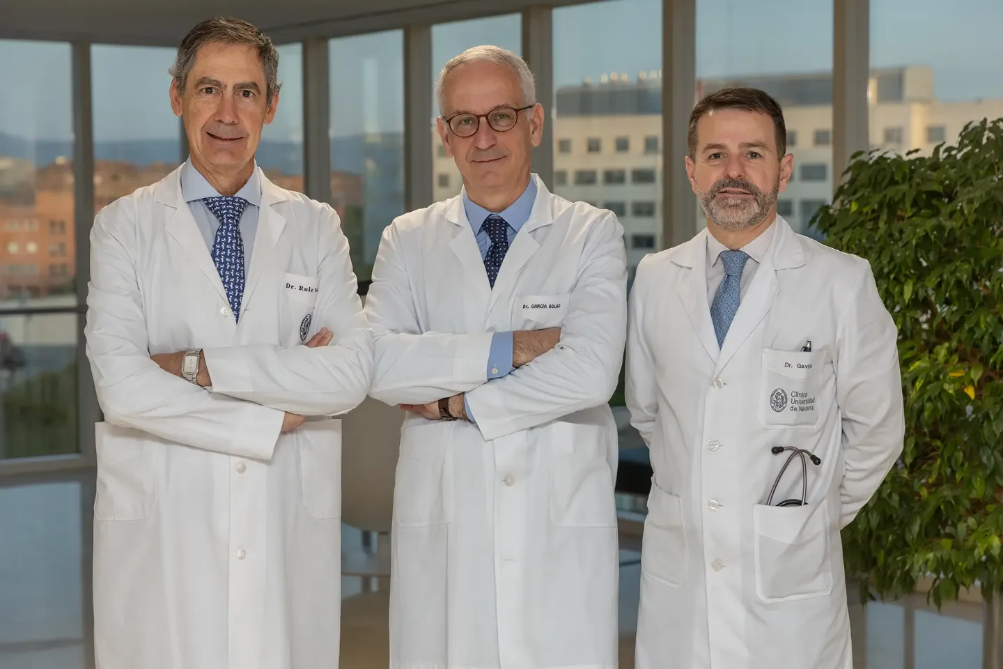 Imagen de tres médicos cardiólogos de la Clínica Universidad de Navarra con sus batas en un pasillo de consultas con una cristalera de fondo.