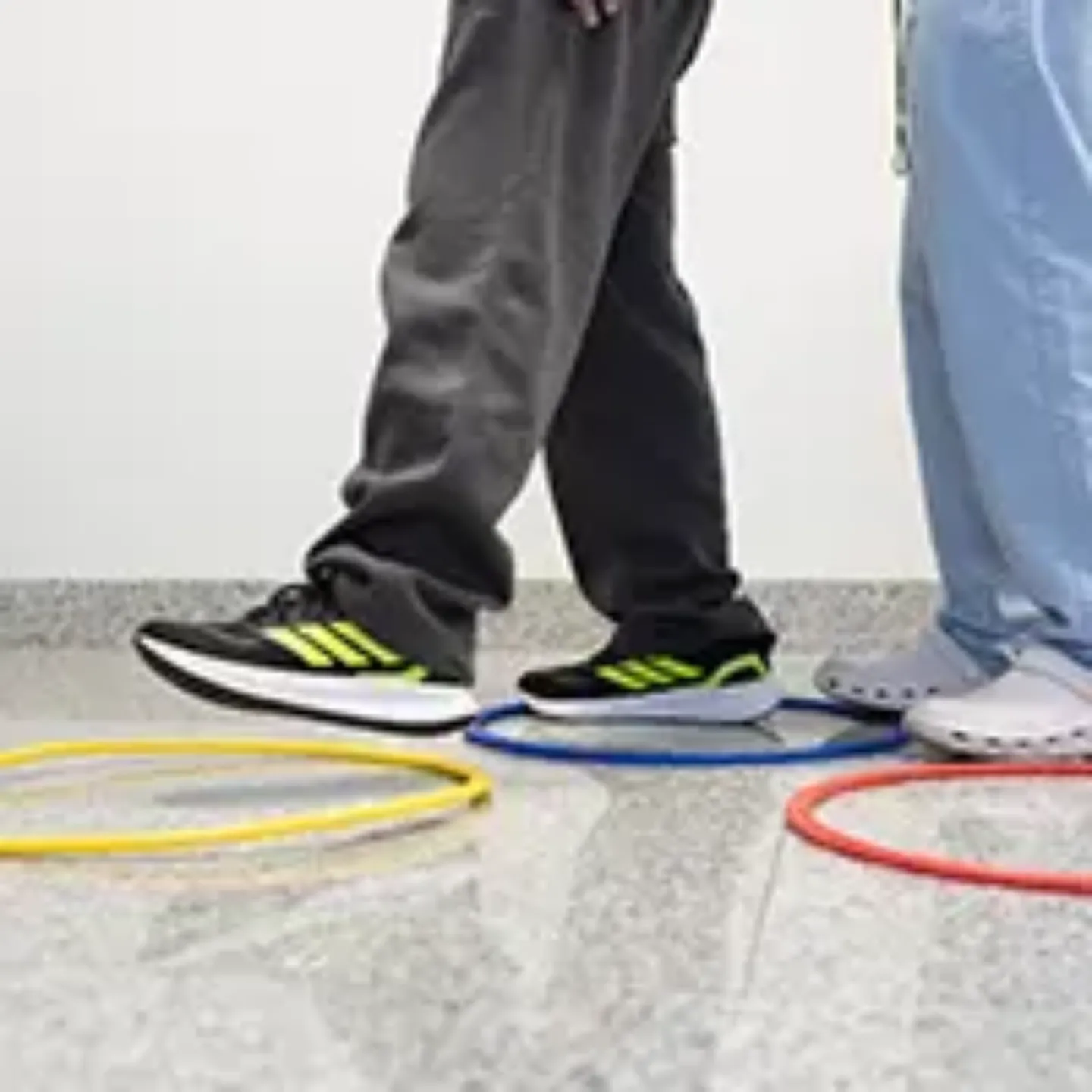 Imagen de unas piernas con zapatillas de deporte caminando entre unos aros colocados en el suelo.