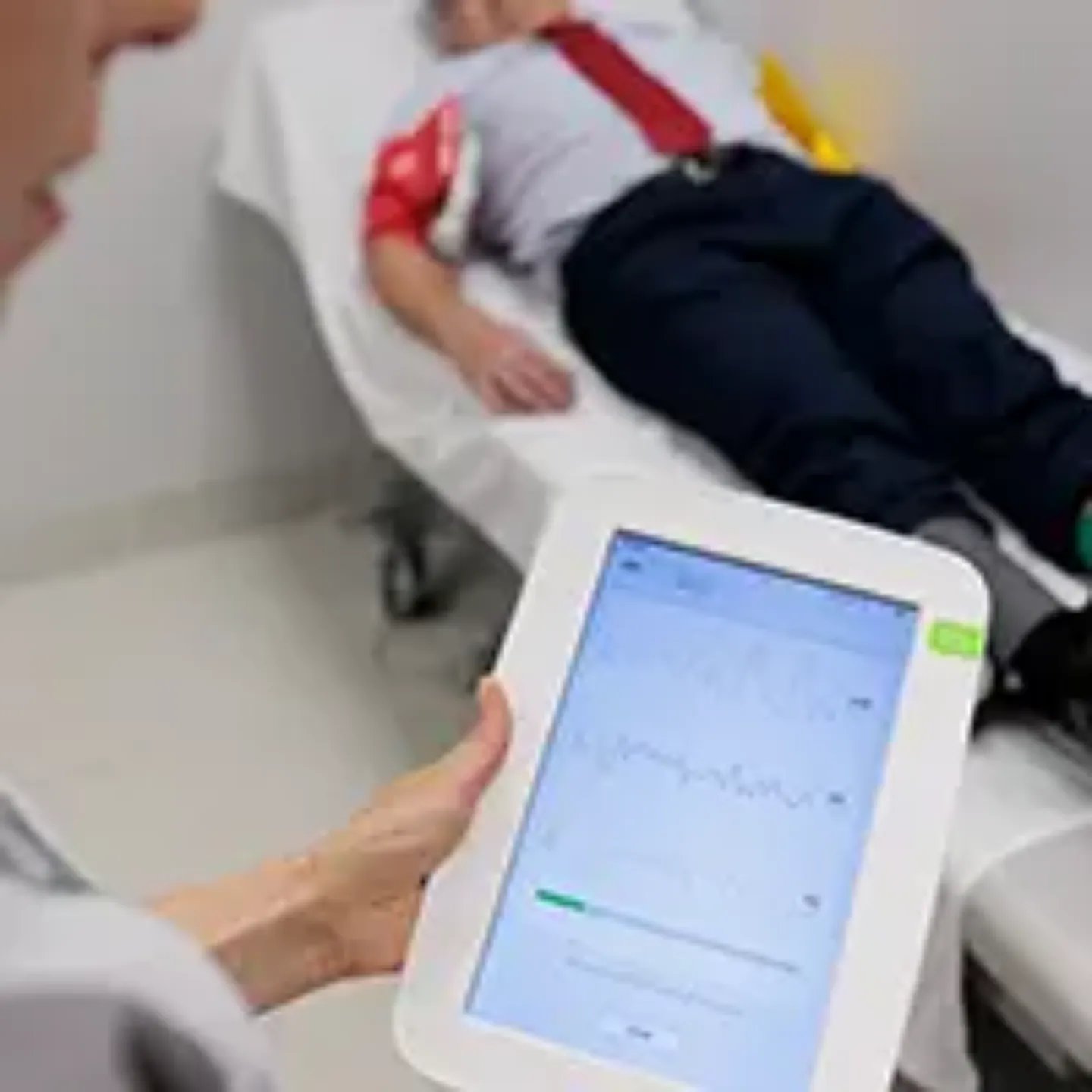 Imagen de un paciente tumbado en una camilla y la pantalla de una tablet digital en primer plano con gráficos de las constantes del paciente. 