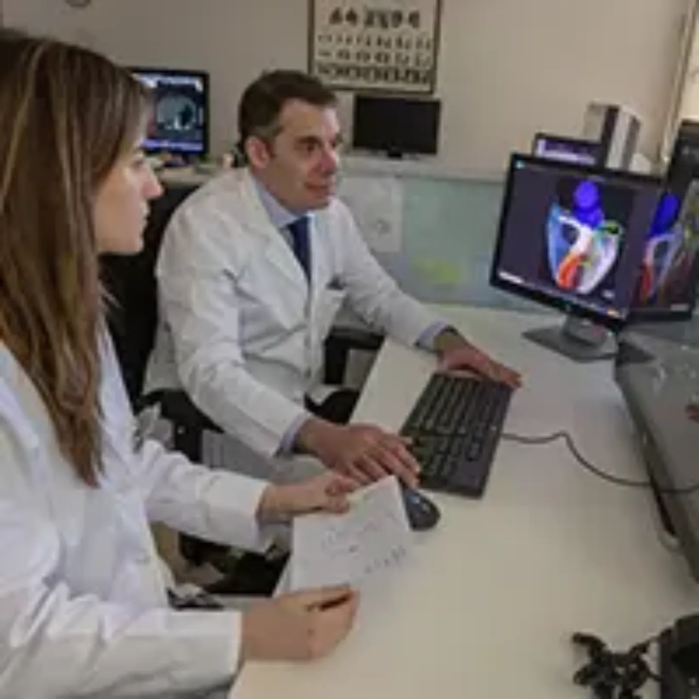 Imagen de dos radiólogos, un hombre y una mujer, en una sala de informes revisando en el ordenador varias imágenes cardiacas.