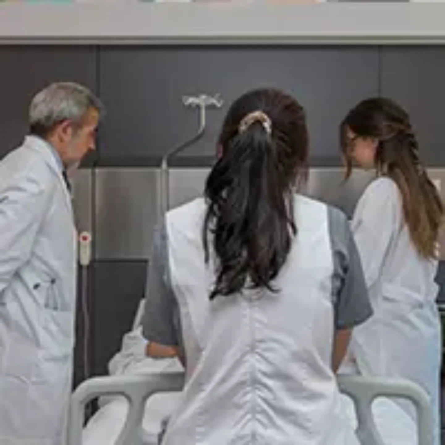 Imagen de dos médicos y una enfermera a pie de cama de un paciente hospitalizado.