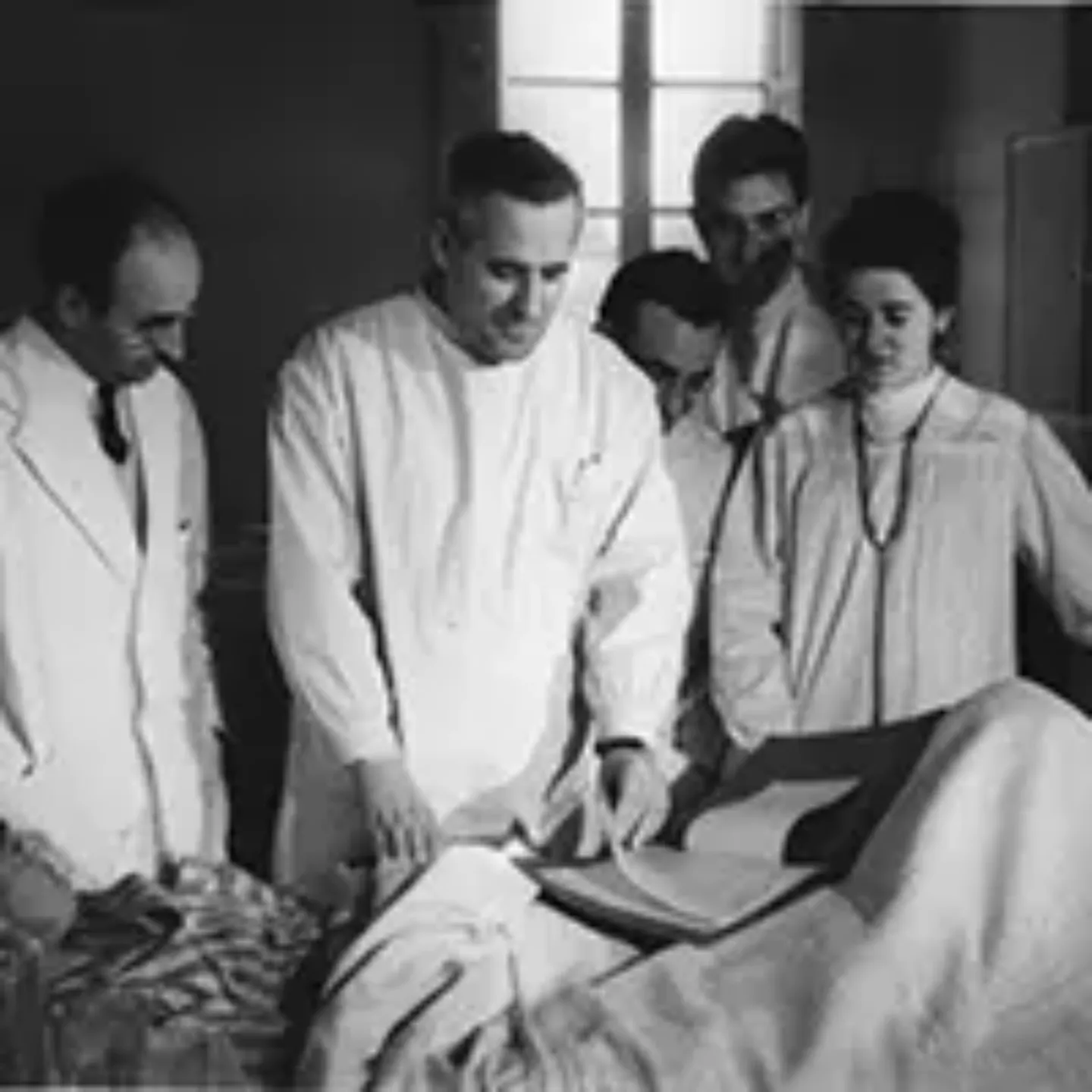 Imagen en blanco y negro de varios médicos de la Clínica atendiendo a un paciente.