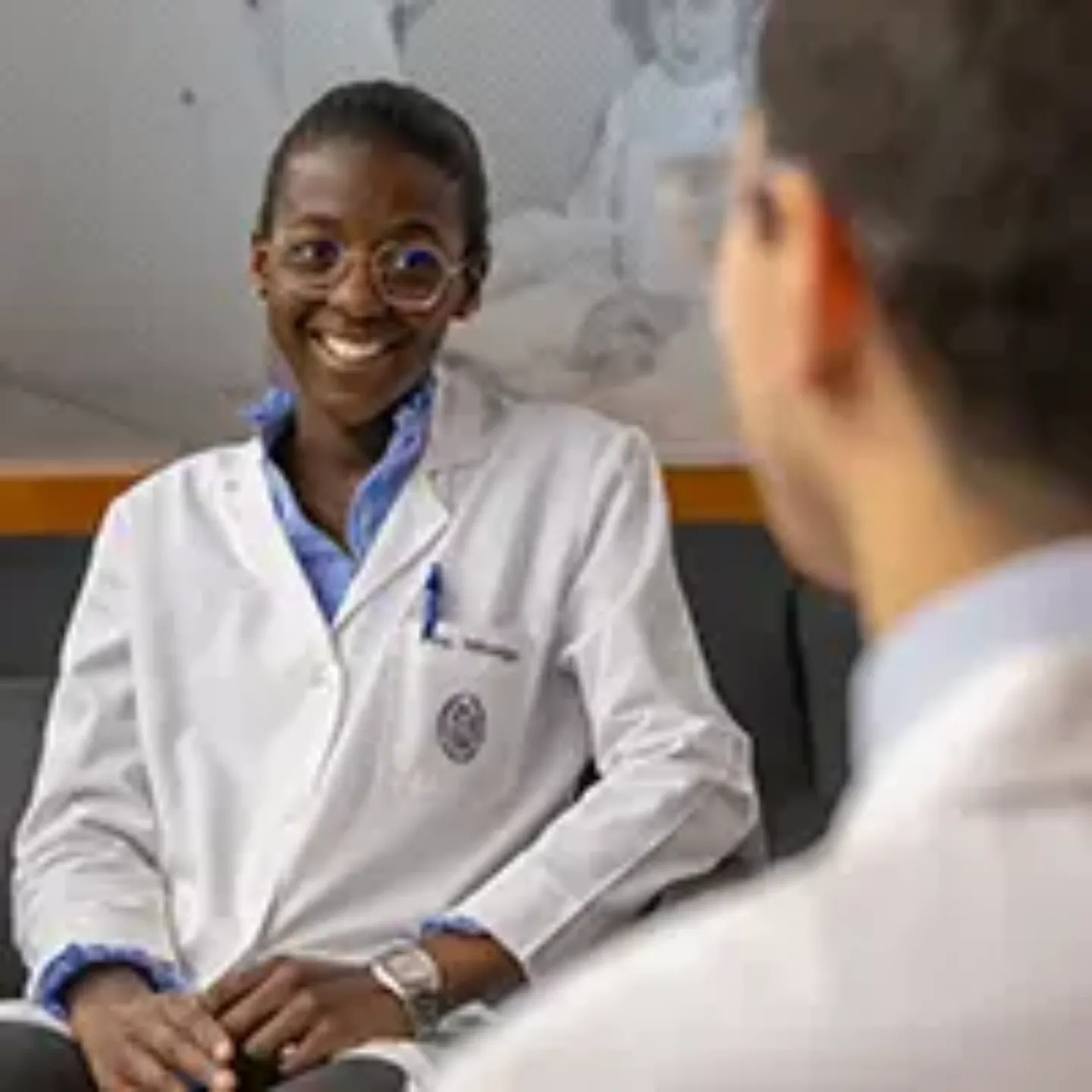 Imagen de Carmen Mbongo y Christian Espinoza, residentes de la Clínica, hablando sentados en unas butacas. Clínica Universidad de Navarra