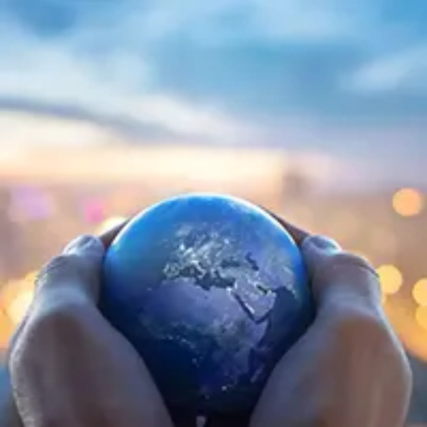 Imagen de unas manos sosteniendo una bola del mundo plateada con un atardecer de fondo.