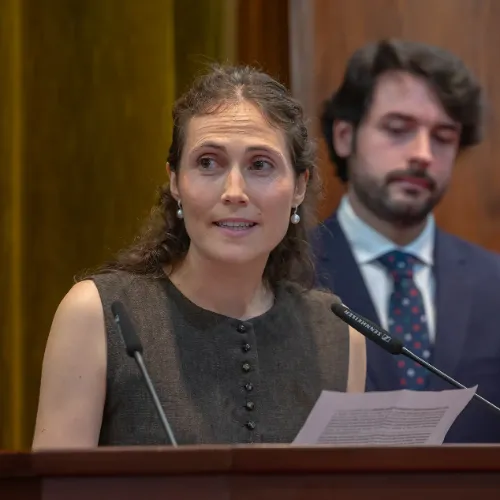 Imagen de una residente dando el discurso de despedida de su promoción y otro compañero en segundo plano.