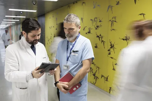 Imagen del Dr. Eduardo Castañón con un técnico revisando un documento en un pasillo de la Clínica Universidad de Navarra en Madrid. 