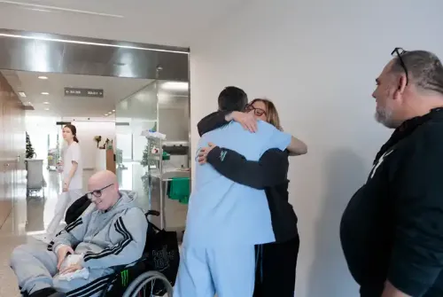 Imagen de Enric, paciente adolescente de la Unidad de Protonterapia de la Clínica Universidad de Navarra, sentado en una silla de ruedas y su madre abrazando a un profesional.