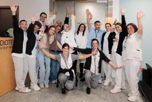 Imagen de Enric, paciente adolescente de la Unidad de Protonterapia de la Clínica Universidad de Navarra, junto a su familia y a los profesionales de la Unidad con los brazos levantados.