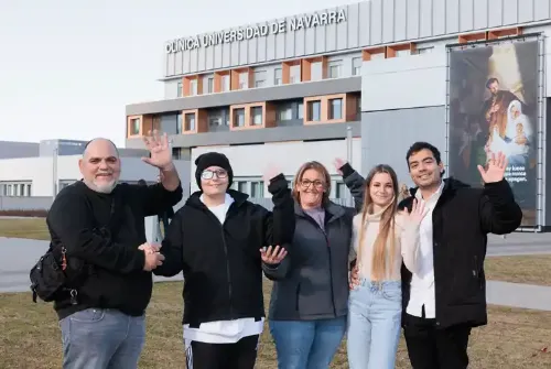 Imagen de Enric, paciente adolescente de la Unidad de Protonterapia de la Clínica Universidad de Navarra, junto con su familia diciendo adiós con las manos en la entrada exterior del hospital.