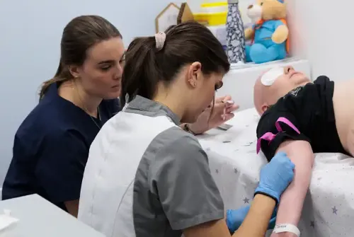 Imagen de Enric, paciente adolescente de la Unidad de Protonterapia de la Clínica Universidad de Navarra, tumbado en una camilla y dos enfermeras colocándole una vía en el brazo.