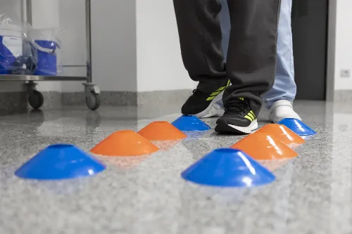 Imagen de un suelo con conos azules y naranjas y unos pies con zapatillas de deporte acercándose a ellos. 