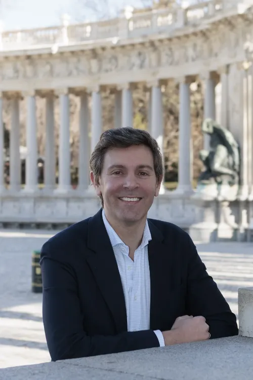 Imagen de un médico cardiólogo sin bata sentado en el parque de El Retiro con una columnata de fondo.