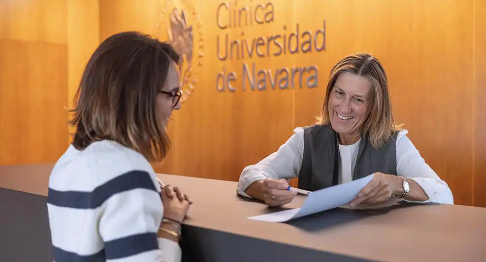 Reputación Merco Empresas 2024. Clínica Universidad de Navarra Imagen de una profesional administrativa atendiendo a una paciente en la entrada de la Clínica Universidad de Navarra en Pamplona.